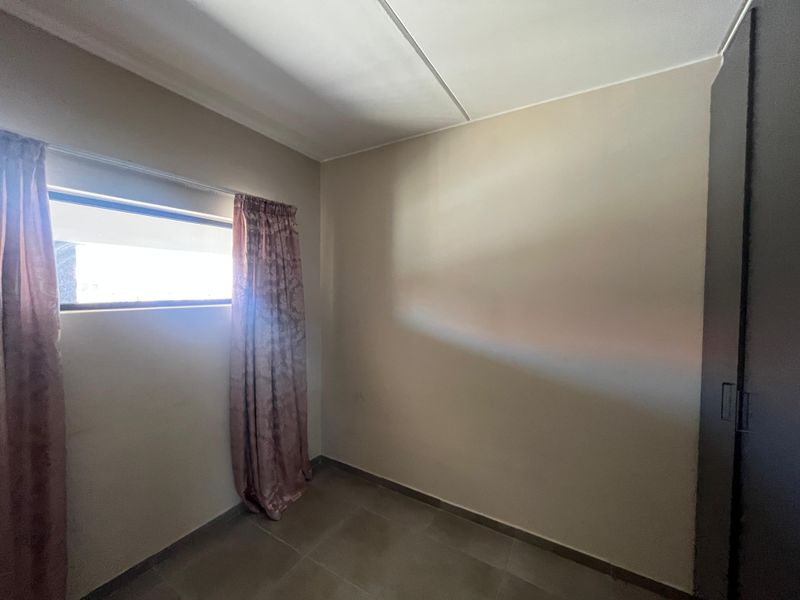 A simple, empty bedroom featuring tiled flooring and a built-in wardrobe, offering a neutral canvas for personalization.