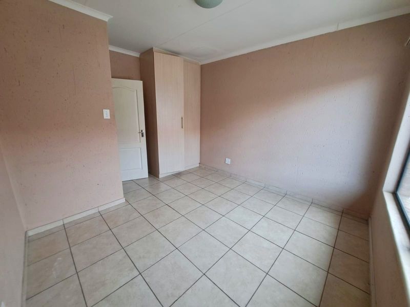 A vacant bedroom featuring neutral tiled flooring, a built-in wardrobe, and painted walls, offering a clean canvas for personalization.