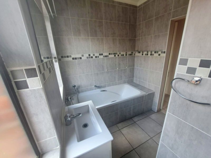 A clean, tiled bathroom featuring a built-in bathtub, a modern vanity basin with chrome fixtures, and neutral wall tiling.