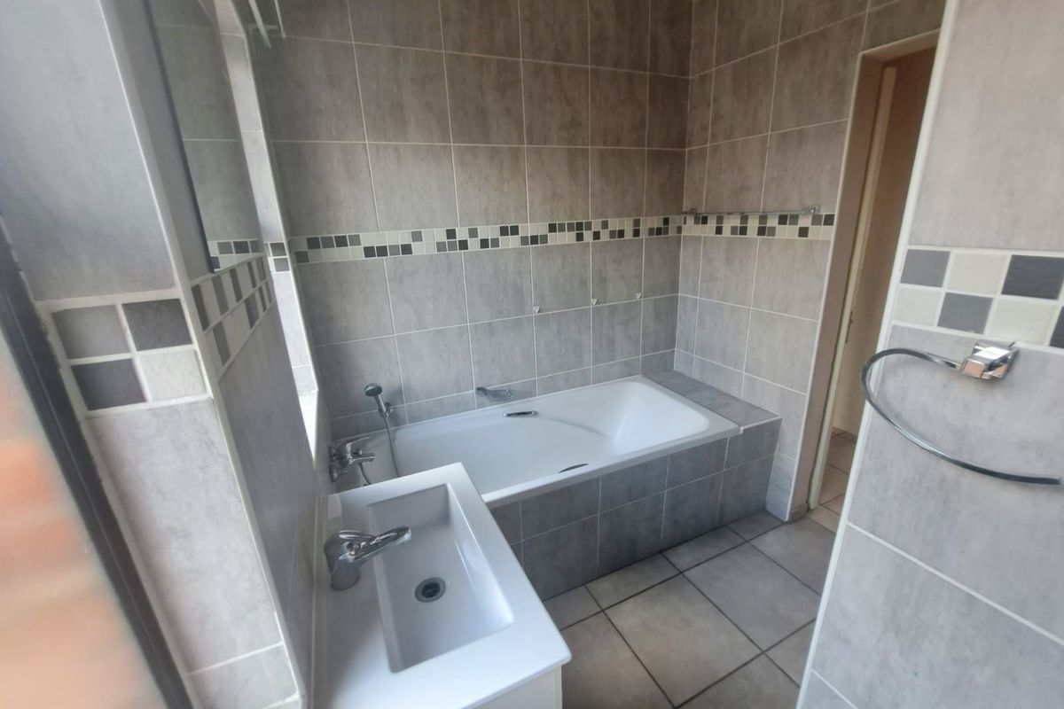 A clean, tiled bathroom featuring a built-in bathtub, a modern vanity basin with chrome fixtures, and neutral wall tiling.