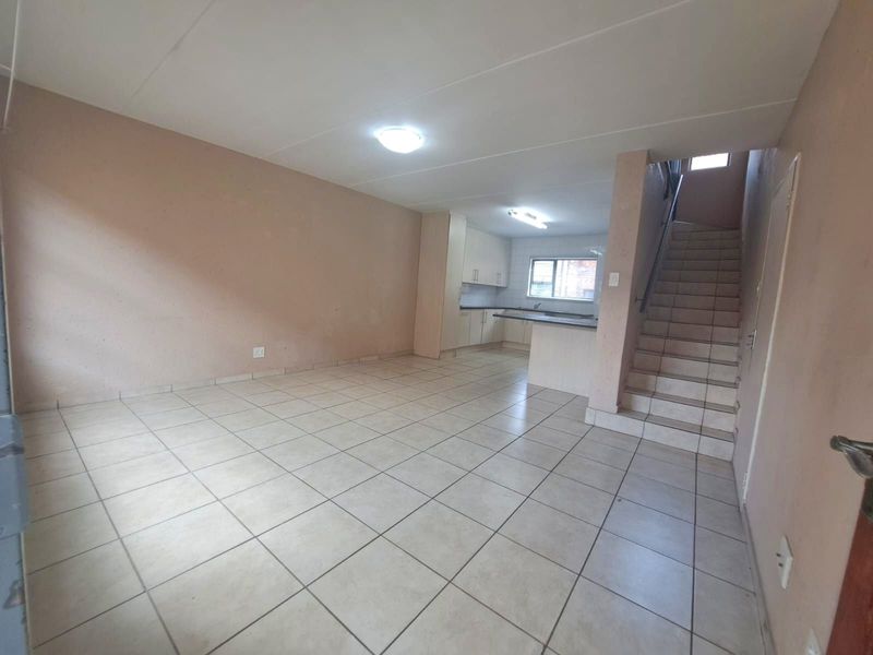Spacious open-plan living and kitchen area featuring tiled flooring, built-in cabinetry, and a staircase leading to the upper level.