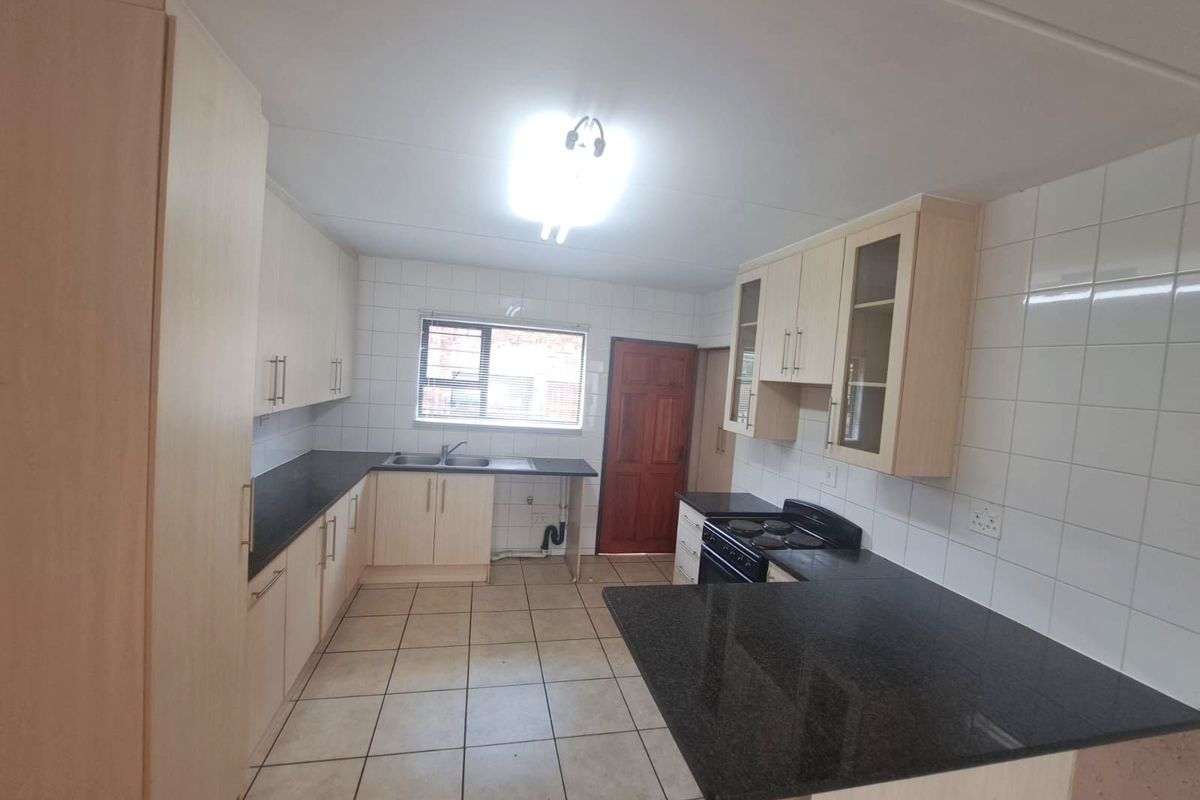 A functional kitchen featuring light laminate cabinetry, dark granite countertops, ceramic tiling, and a freestanding stove with direct access to an exterior door.