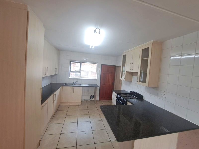 A functional kitchen featuring light laminate cabinetry, dark granite countertops, ceramic tiling, and a freestanding stove with direct access to an exterior door.