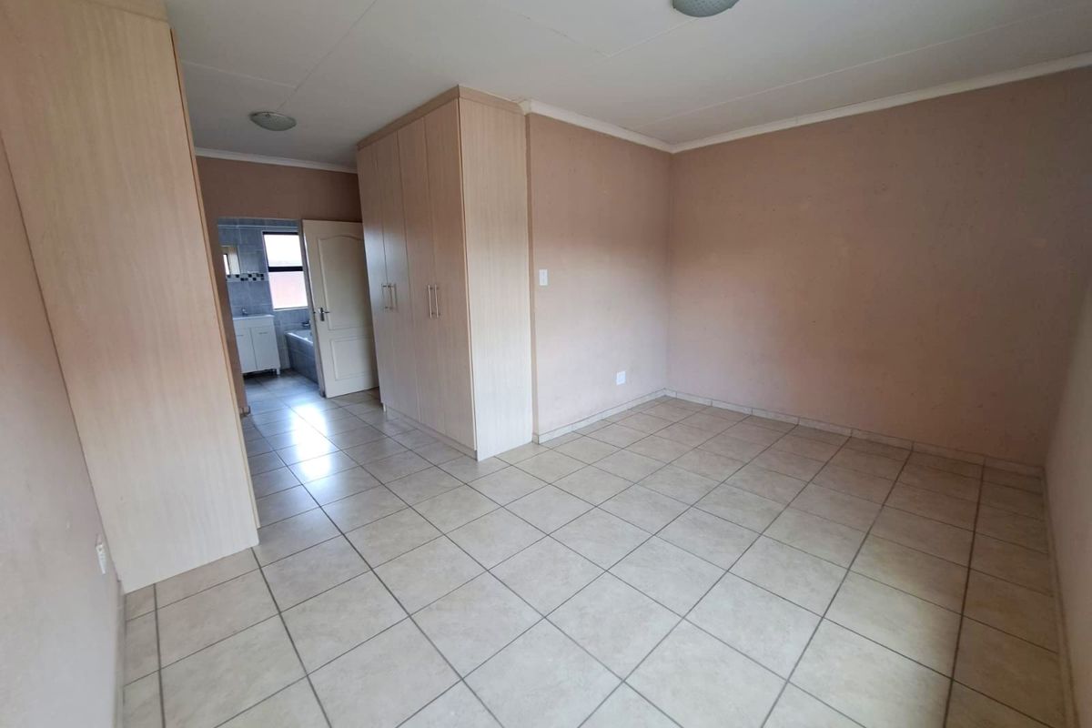 An empty bedroom featuring neutral tiled flooring and built-in wooden cupboards, with an adjacent view into a bathroom area.