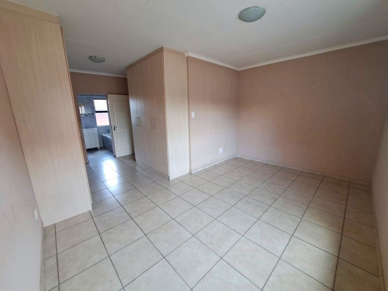 An empty bedroom featuring neutral tiled flooring and built-in wooden cupboards, with an adjacent view into a bathroom area.
