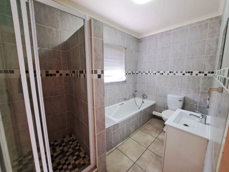 A functional bathroom featuring a separate shower enclosure, built-in bathtub, toilet, and a vanity basin with neutral wall and floor tiling.