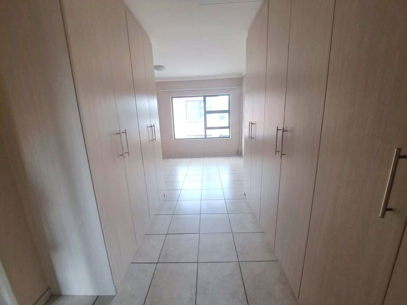 A bright, empty bedroom featuring extensive built-in cupboards and neutral tiled flooring, offering a clean and versatile space.