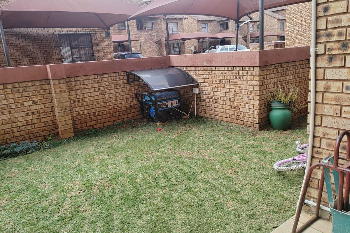 A private rear garden area featuring a brick boundary wall, lawn space, and a fixed outdoor generator shelter.