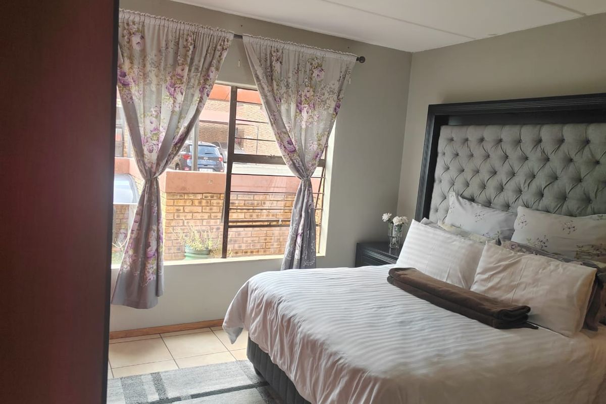A bedroom featuring tiled flooring, a large window with security bars, and a neutral wall finish.