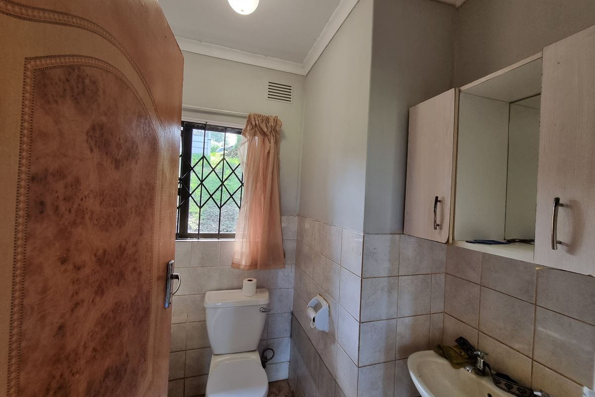 A functional bathroom featuring a standard toilet, wall-mounted vanity cabinet, and tiled walls with a security-grille window.