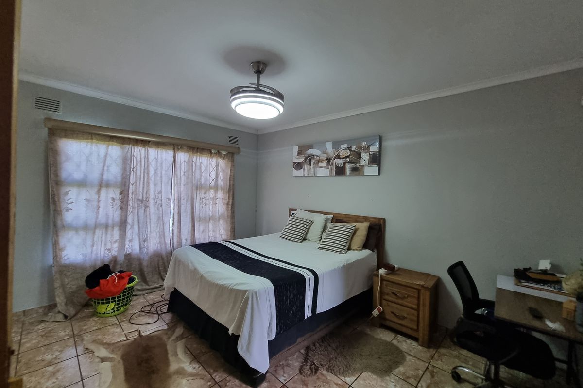 A bedroom featuring tiled flooring, a ceiling fan with integrated light, and large windows with security bars.