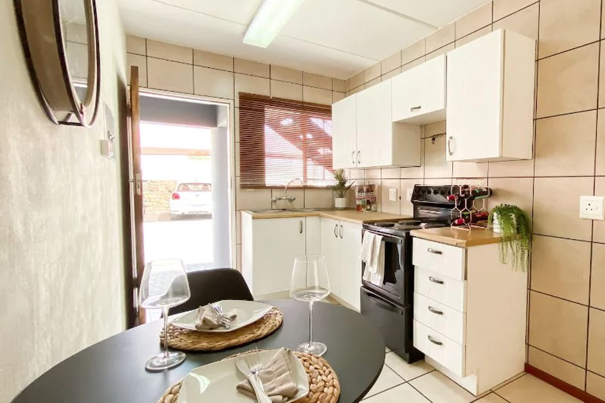 Compact kitchen featuring white cabinetry, tiled walls, and built-in oven, with direct access to the exterior parking area.