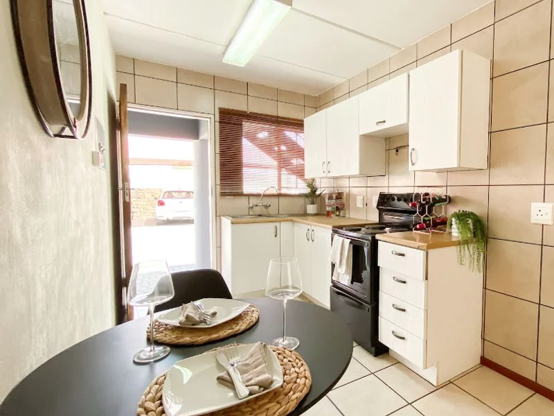 Compact kitchen featuring white cabinetry, tiled walls, and built-in oven, with direct access to the exterior parking area.