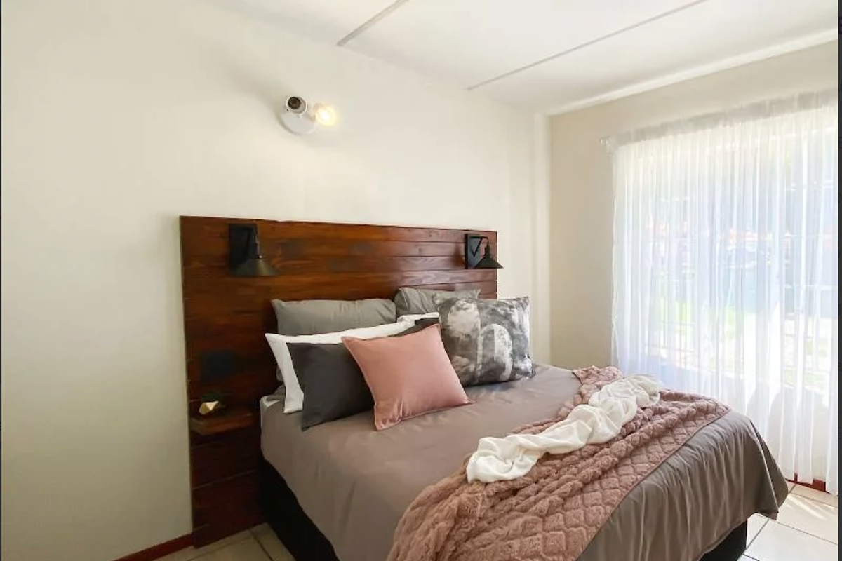 A well-lit bedroom featuring a custom built-in wooden headboard with integrated lighting and neutral tiled flooring.