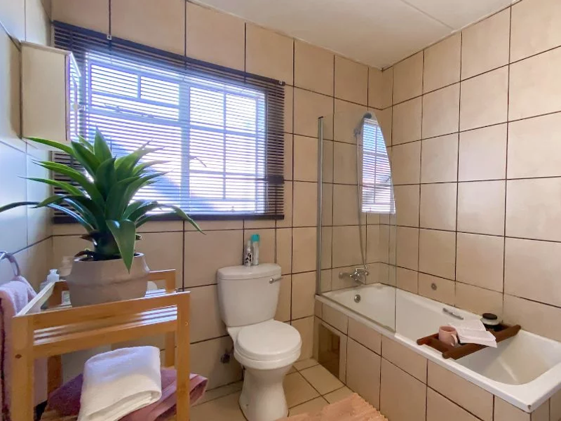 A functional bathroom featuring a bathtub with a glass shower screen, a toilet, and neutral wall tiling throughout.