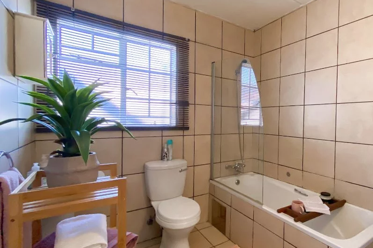 A functional bathroom featuring a bathtub with a glass shower screen, a toilet, and neutral wall tiling throughout.