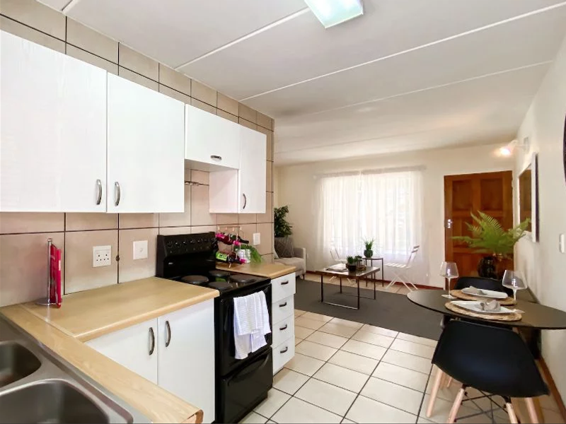 Open-plan kitchen and living area featuring white cabinetry, laminate countertops, tiled flooring, and a functional layout suitable for modern apartment living.