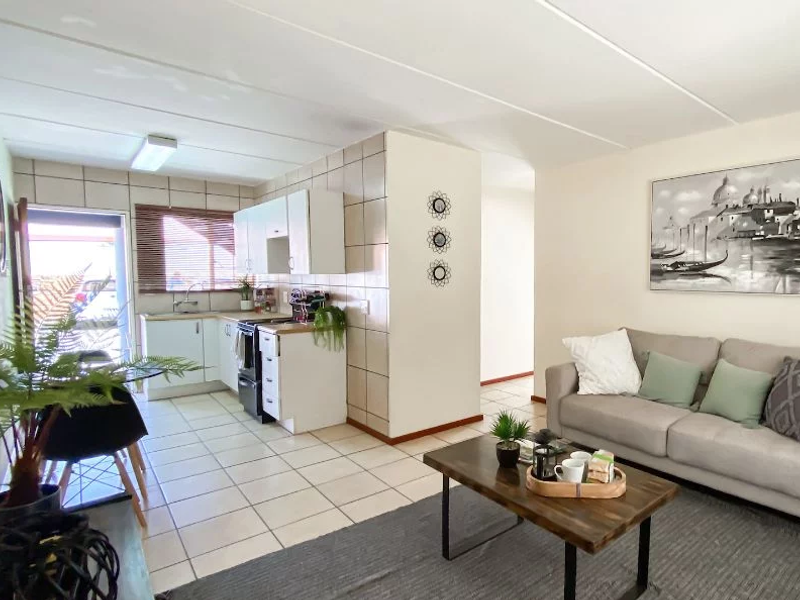 Open-plan living area featuring a functional kitchen with tiled splashbacks and cabinetry, seamlessly flowing into a comfortable lounge space with tiled flooring.