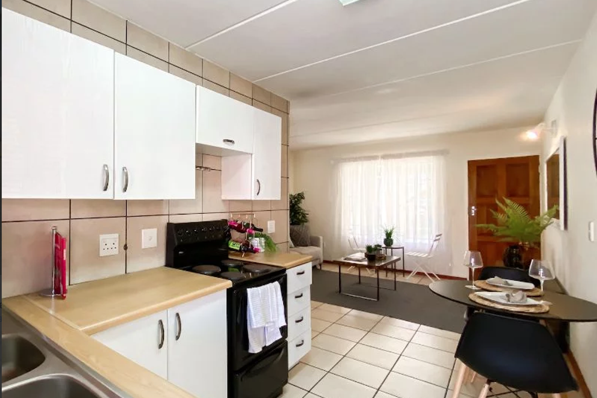 Open-plan kitchen and living area featuring white cabinetry, laminate countertops, tiled flooring, and a functional layout suitable for modern apartment living.