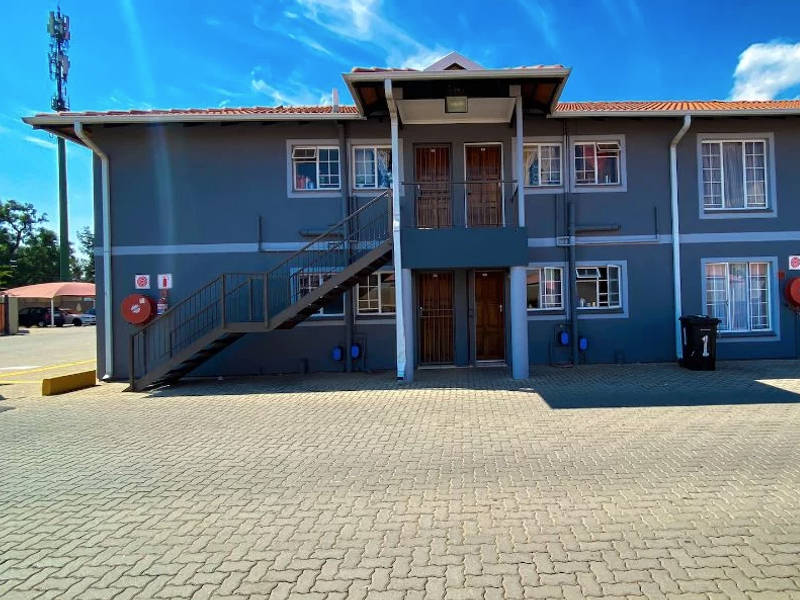 Front elevation of a multi-story apartment building featuring a paved driveway, external staircase, and secure access points.