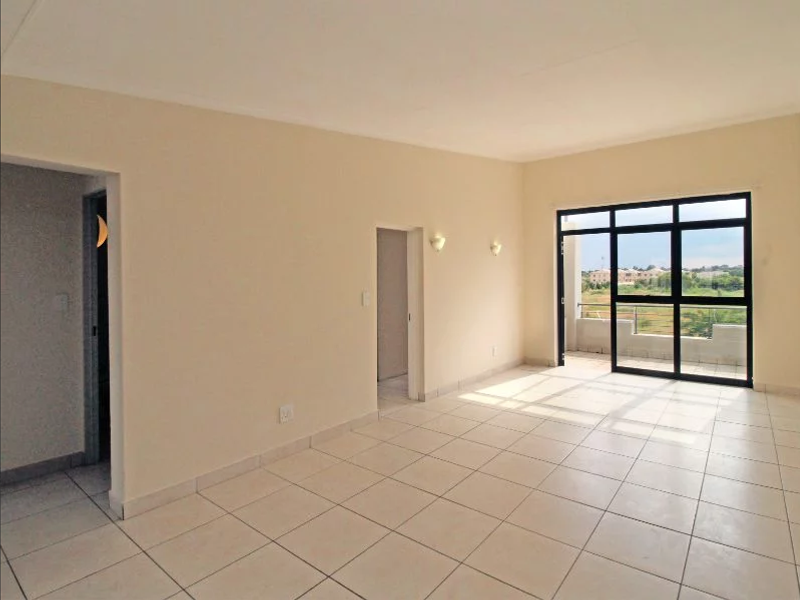 A bright, empty living room featuring neutral tiled flooring and a large sliding glass door that opens onto a balcony with scenic views.