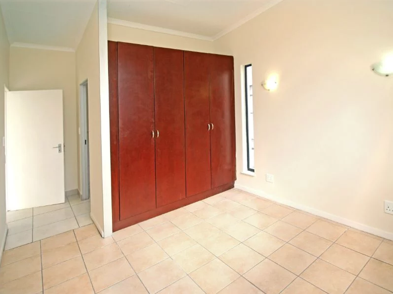 An empty bedroom featuring tiled flooring, built-in wooden cupboards, and wall-mounted lighting fixtures.