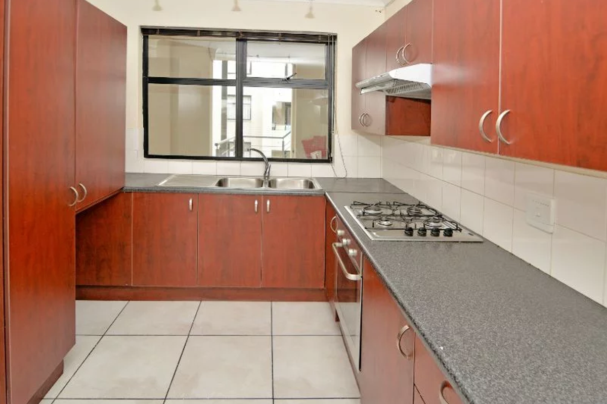 A functional kitchen featuring wood-finish cabinetry, granite countertops, a gas hob, built-in oven, and tiled flooring with a neutral backsplash.