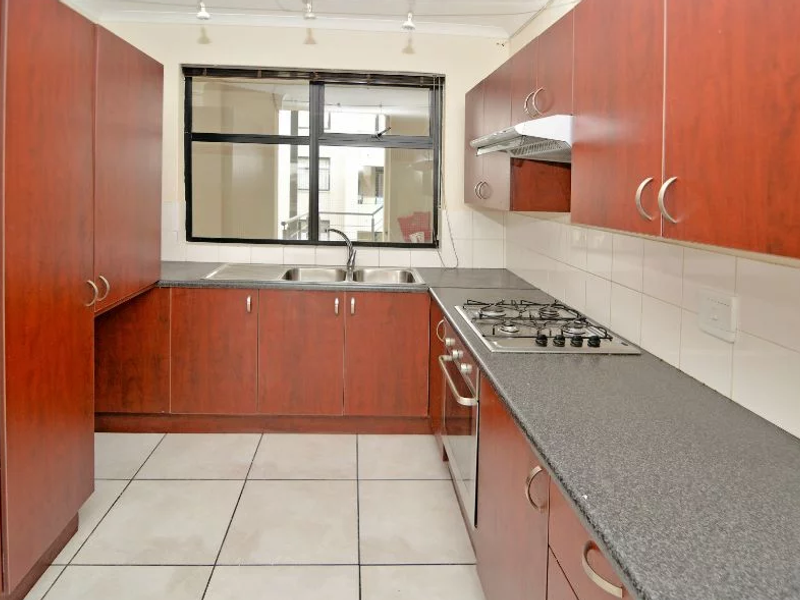 A functional kitchen featuring wood-finish cabinetry, granite countertops, a gas hob, built-in oven, and tiled flooring with a neutral backsplash.