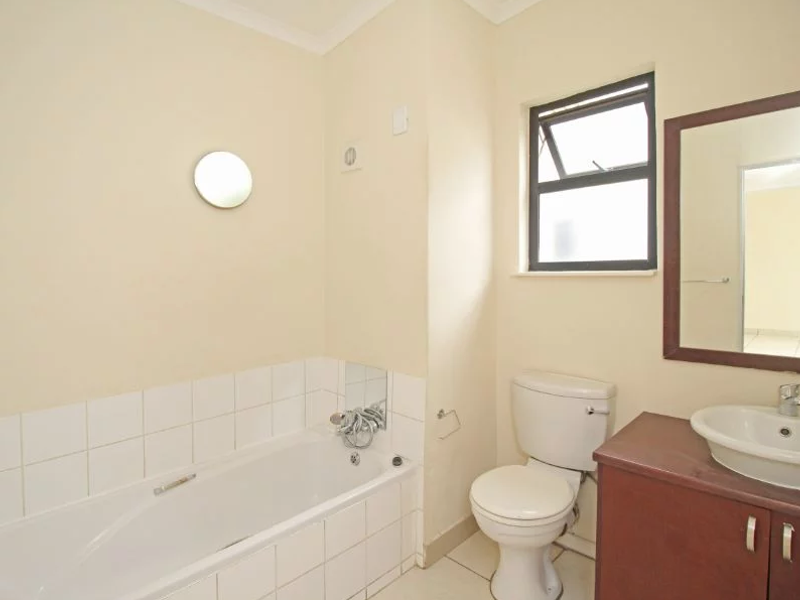 A functional bathroom featuring a bathtub, a standard toilet, and a vanity cabinet with a basin, finished with neutral wall tones and tiled splashbacks.