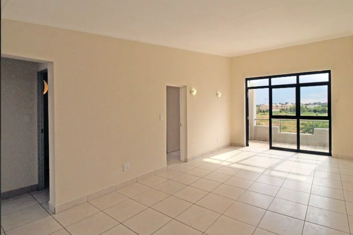A bright, empty living room featuring neutral tiled flooring and a large sliding glass door that opens onto a balcony with scenic views.