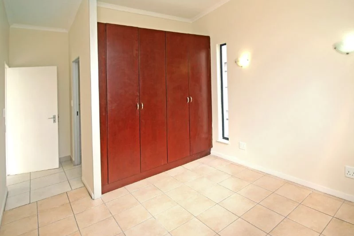 An empty bedroom featuring tiled flooring, built-in wooden cupboards, and wall-mounted lighting fixtures.