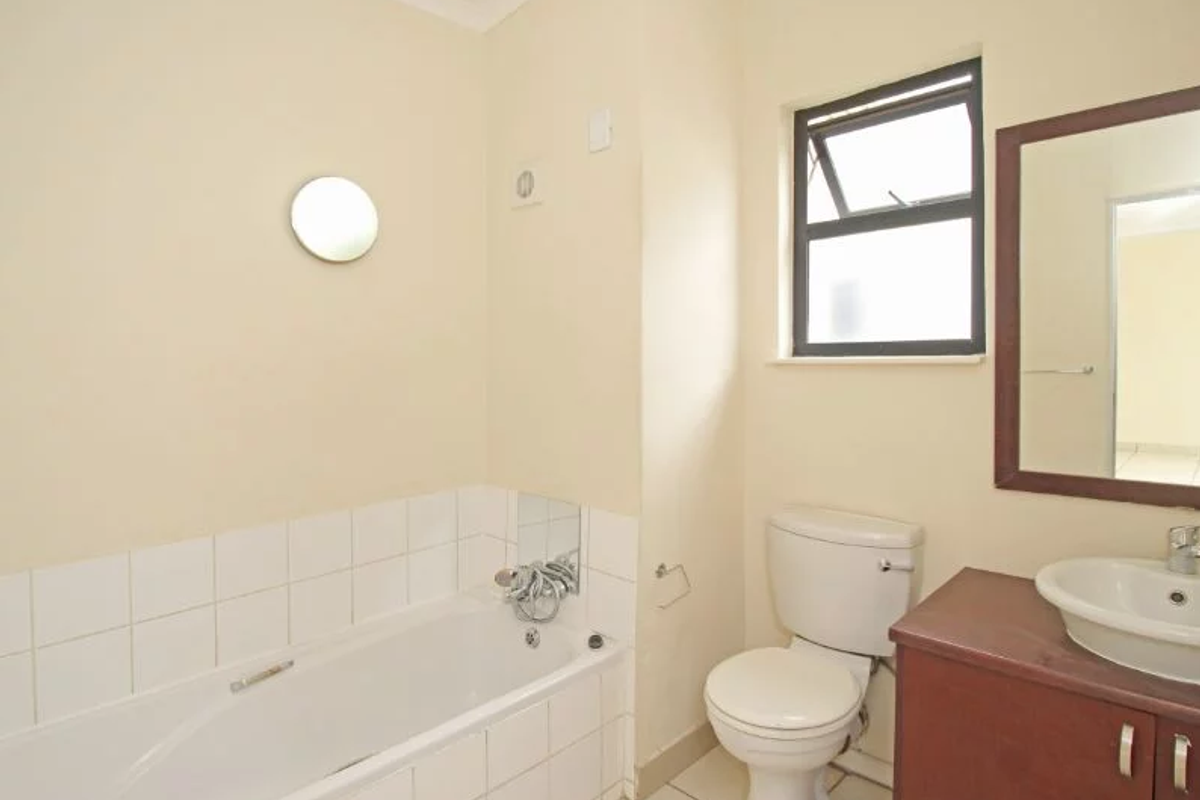A functional bathroom featuring a bathtub, a standard toilet, and a vanity cabinet with a basin, finished with neutral wall tones and tiled splashbacks.