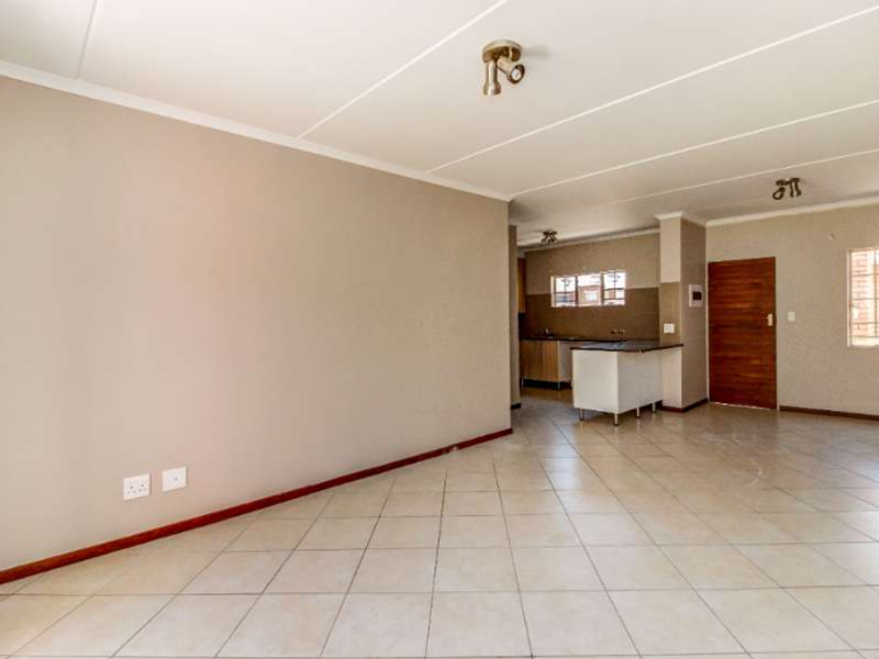 Spacious open-plan living area featuring tiled flooring, neutral walls, and an integrated kitchen space with cabinetry and countertop.