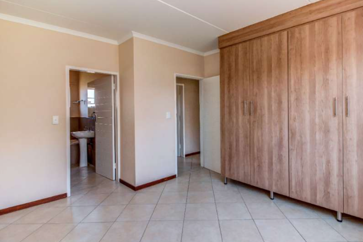 A spacious bedroom featuring neutral walls, tiled flooring, and extensive built-in wooden cupboards, with direct access to an en-suite bathroom.