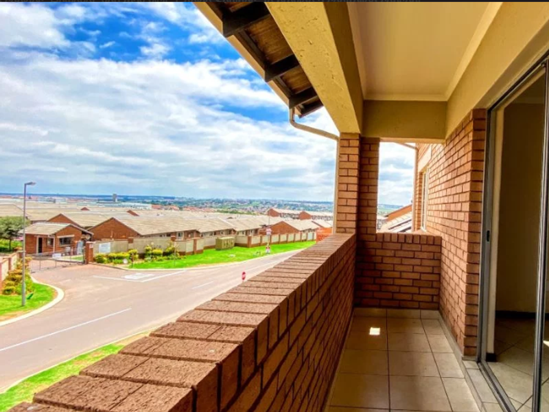 A covered balcony featuring exposed brick walls and tiled flooring, offering an elevated view of the surrounding residential complex and street.