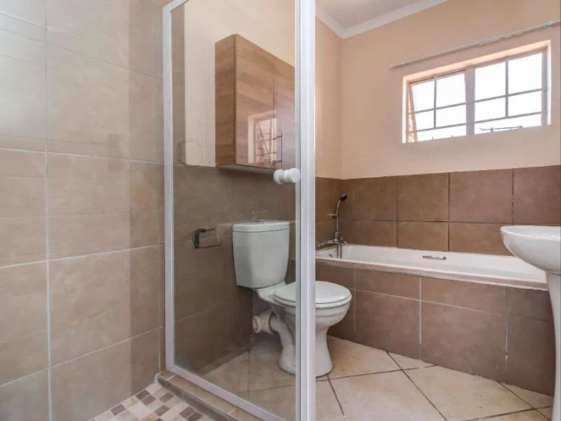 A functional bathroom featuring a shower enclosure, bathtub, pedestal basin, and wall-mounted storage cabinet with neutral tiled finishes.