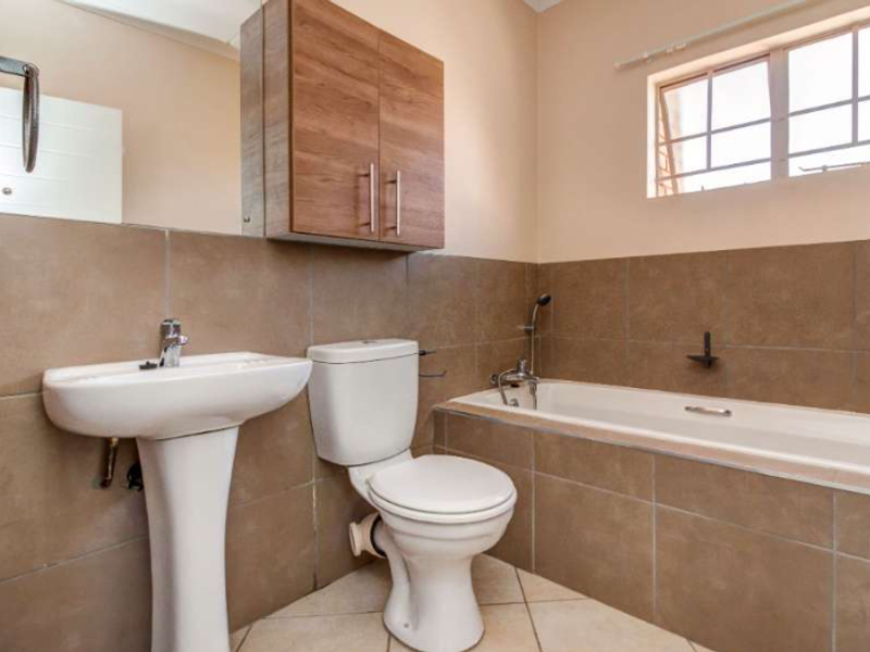 A clean, functional bathroom featuring a pedestal basin, toilet, bathtub, and wall-mounted storage cabinet with neutral wall and floor tiling.