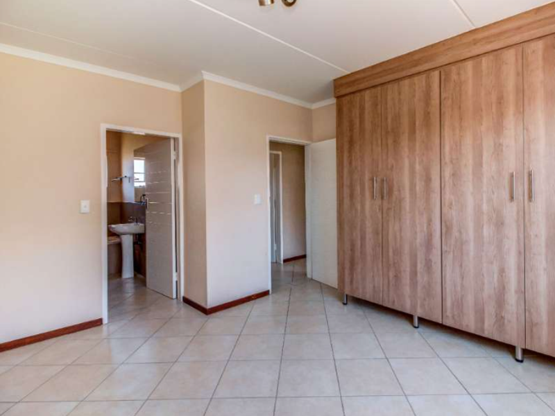 A spacious bedroom featuring neutral walls, tiled flooring, and extensive built-in wooden cupboards, with direct access to an en-suite bathroom.