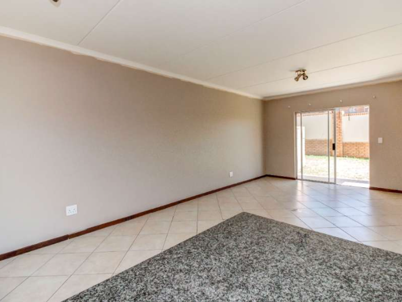 A spacious, empty living area featuring neutral walls, tiled flooring, and a sliding glass door providing access to the exterior.