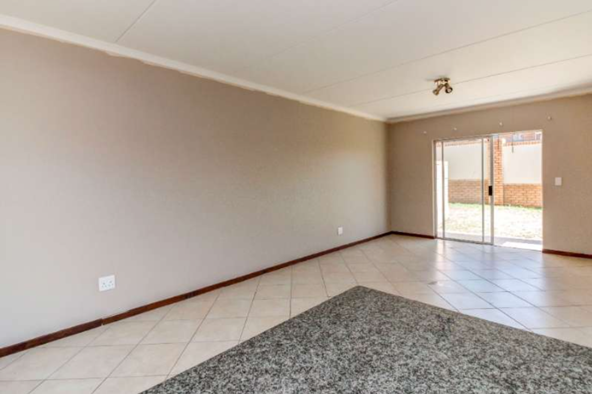 A spacious, empty living area featuring neutral walls, tiled flooring, and a sliding glass door providing access to the exterior.