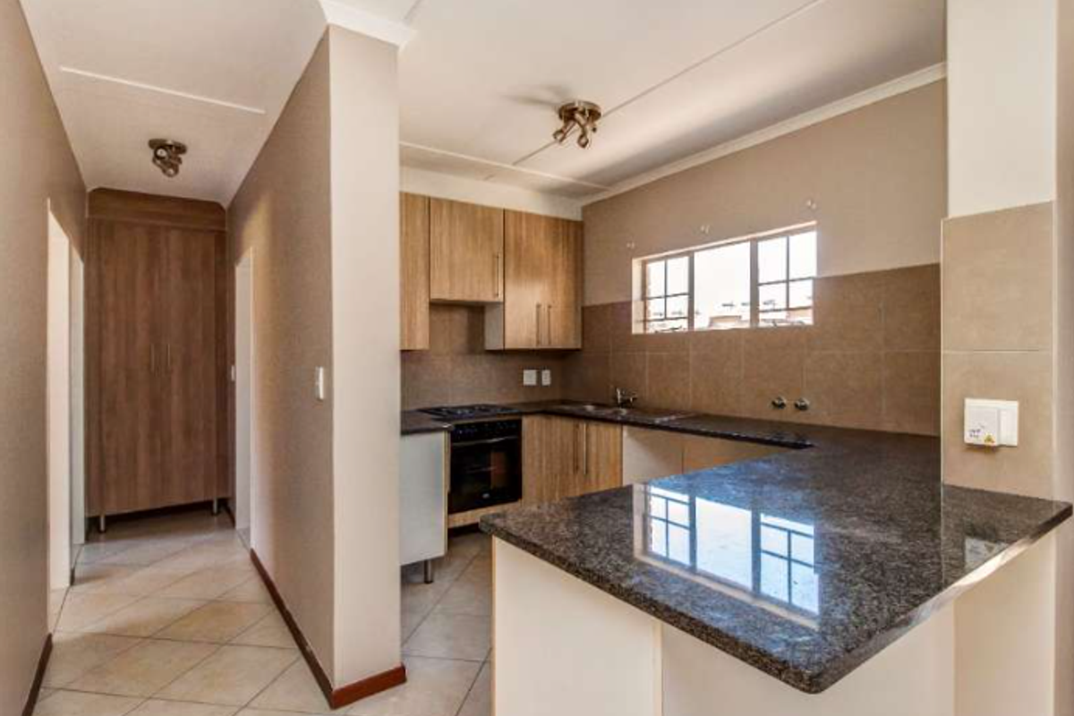 A functional kitchen featuring granite countertops, built-in cabinetry, a hob, and an oven, with an open-plan layout connecting to the hallway.