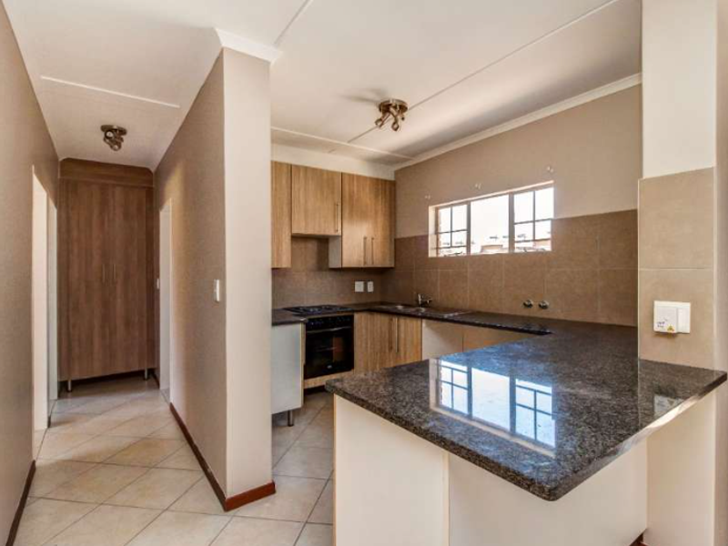 A functional kitchen featuring granite countertops, built-in cabinetry, a hob, and an oven, with an open-plan layout connecting to the hallway.