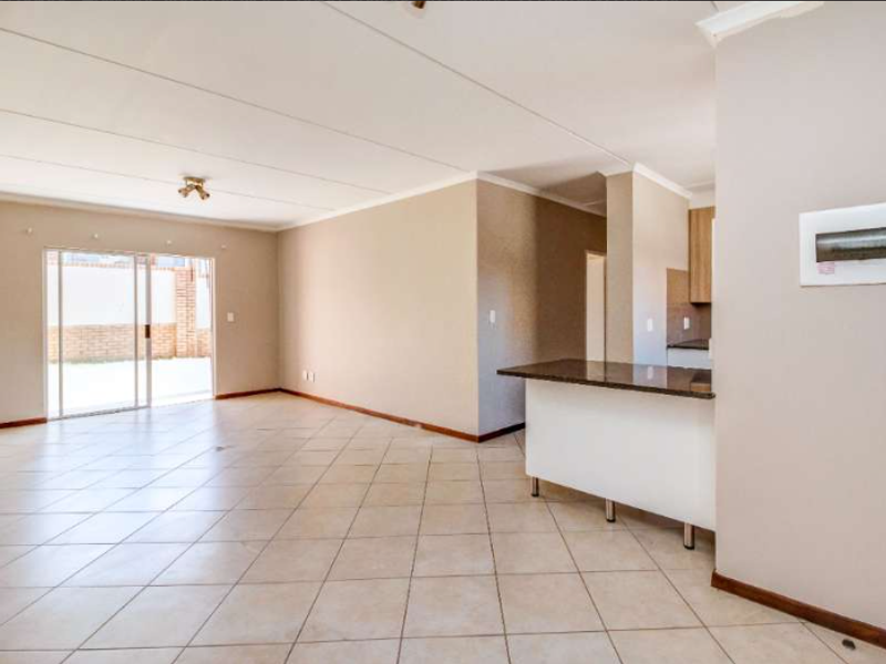 Spacious open-plan living area featuring tiled flooring, a breakfast bar, and sliding glass doors leading to an outdoor space.