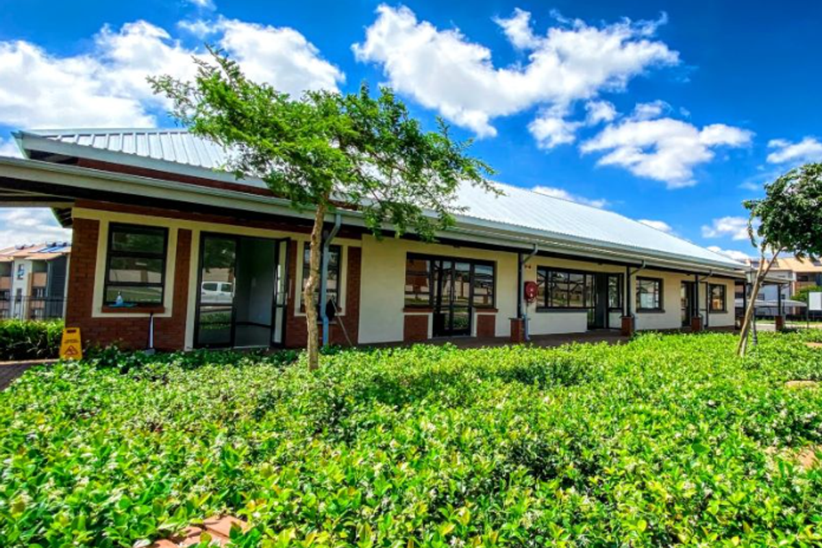 A well-maintained exterior view of the apartment building featuring a metal roof, brick and plaster facade, and landscaped garden area.