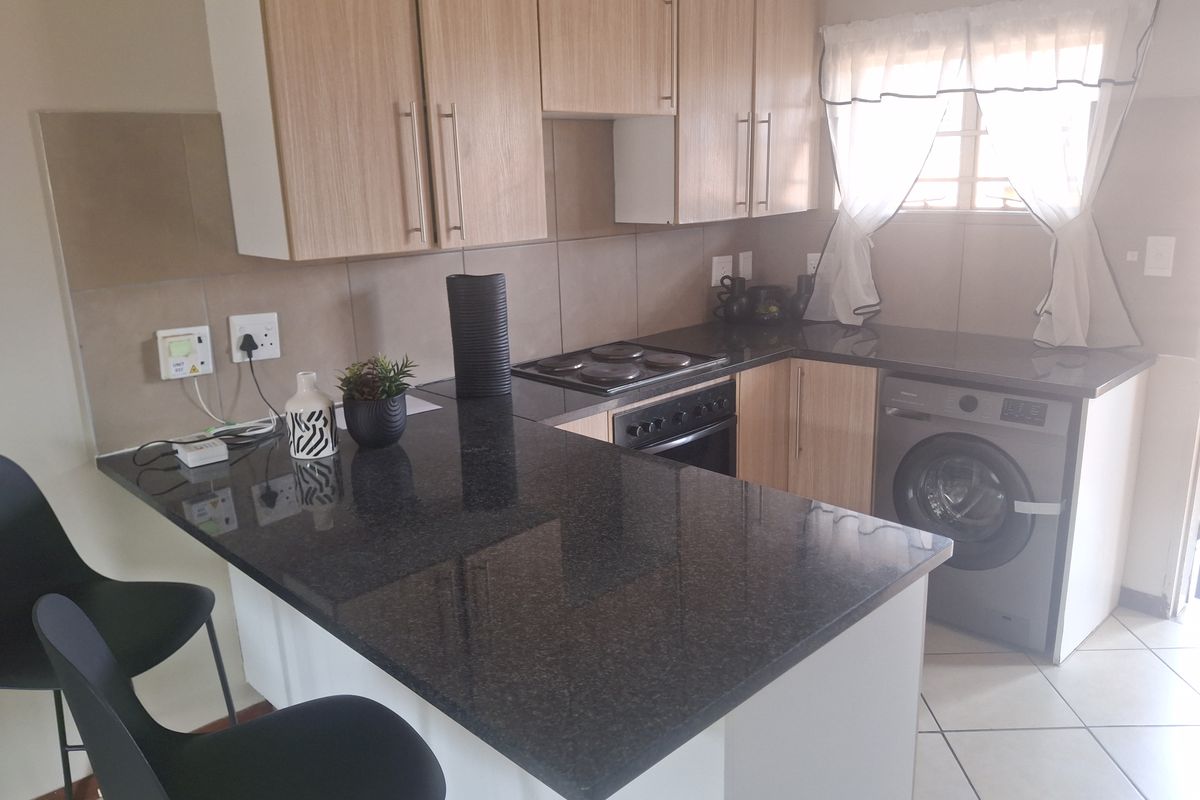 Functional kitchen featuring granite countertops, built-in oven, electric hob, and light wood cabinetry with an integrated washing machine.