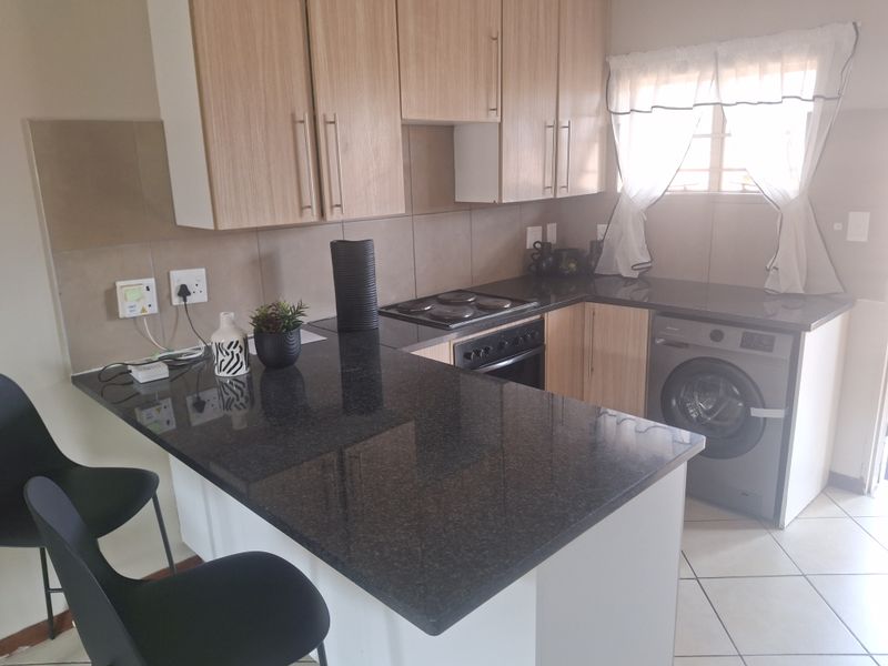 Functional kitchen featuring granite countertops, built-in oven, electric hob, and light wood cabinetry with an integrated washing machine.