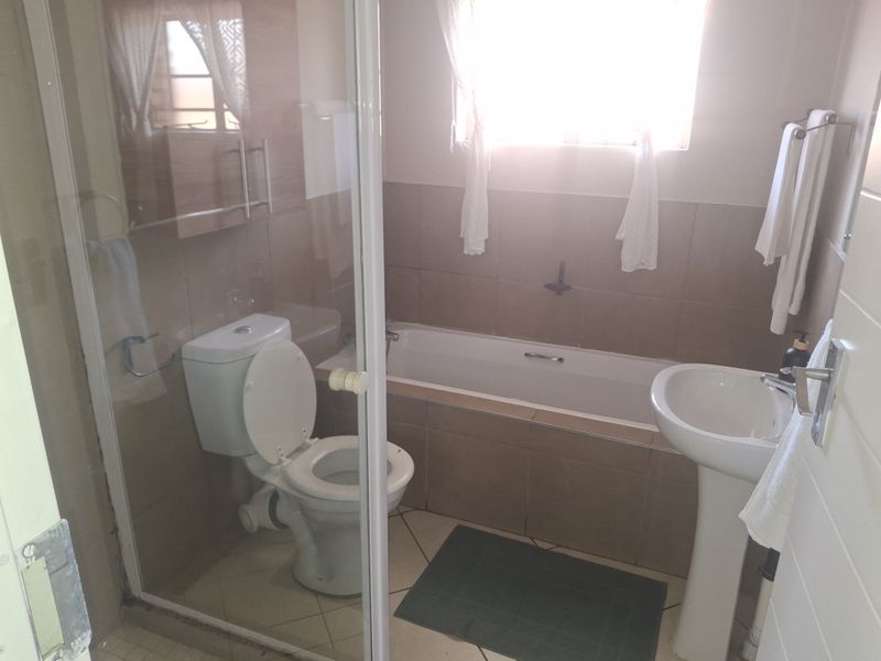 A functional bathroom featuring a pedestal basin, toilet, and a combined bathtub with a glass shower enclosure, finished with neutral wall and floor tiling.