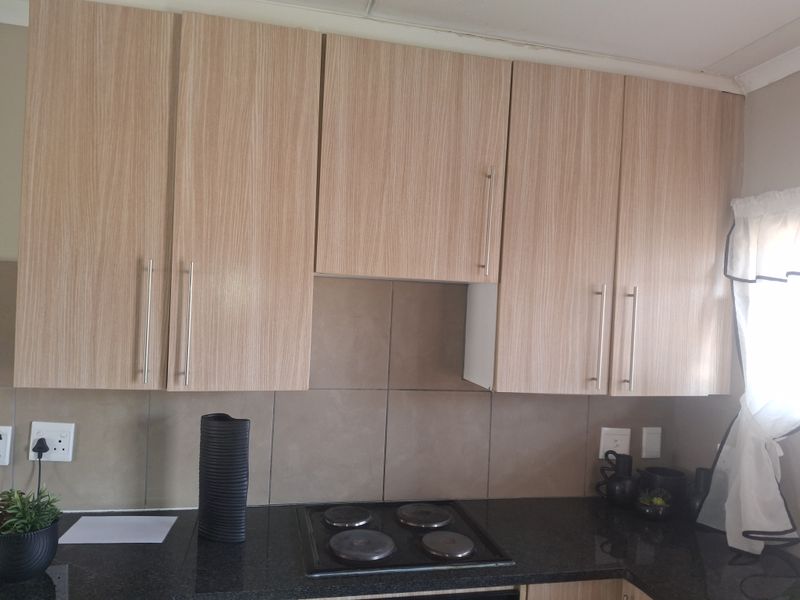 A functional kitchen area featuring light wood-grain cabinetry, a dark granite countertop, and a built-in electric hob with a tiled splashback.