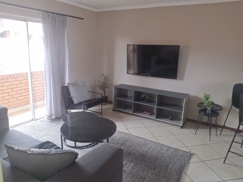 A living room featuring ceramic floor tiles and a sliding glass door providing access to an outdoor balcony area.