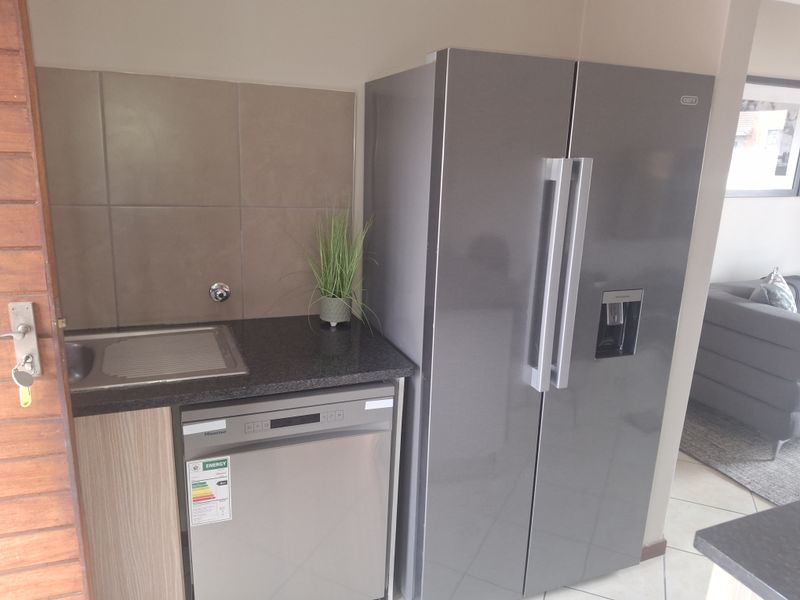 A compact scullery area featuring a stainless steel sink, granite countertop, tiled splashback, and built-in cabinetry with space for a dishwasher.